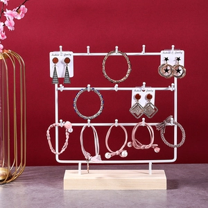 Three-tier white metal jewelry organizer with wooden base on a red and marble surface