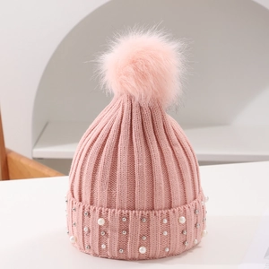 Close-up of pink knit hat featuring faux fur pom-pom and white pearl embellishments