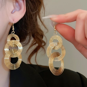 Detailed view of layered gold circular dangle earrings on model and held by hand
