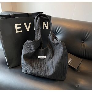 Detail einer schwarzen Plissee-Nylontasche mit Kiss Yourself Label auf Ledersofa
