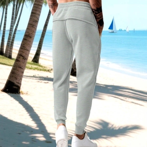 Men's grey jogger pants with knit texture and elastic waist shown on a beach setting