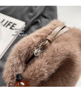 Detail of plush brown bucket bag featuring a smooth metal zipper and amber bead accent