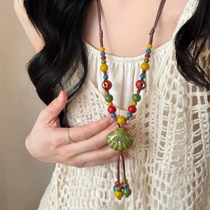 Détail d'un collier bohème en perles de céramique avec pendentif coquillage vert