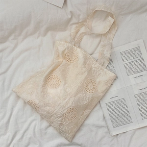 Close-up of beige crochet lace tote bag with floral embroidery on white bedsheet