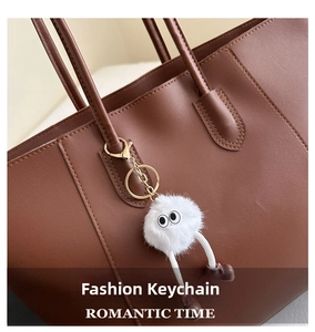 Detail of white fluffy faux fur eyeball charm with gold ring on brown leather tote bag