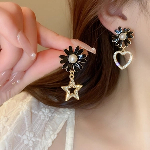 Close-up of asymmetrical black daisy earrings with heart and star charms on a model