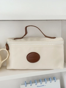 Cream nylon makeup bag with leather logo and brown handle on a minimalist white shelf