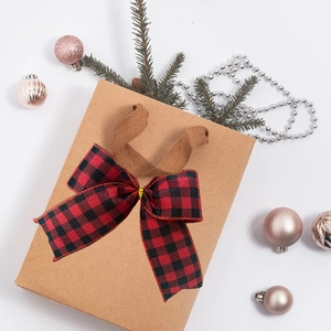 Macro detail of red and black buffalo plaid bow on kraft paper gift bag for Christmas