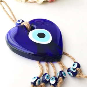 Detailed close-up of heart-shaped glass Evil Eye pendant with blue bead tassels and hemp rope
