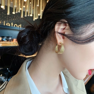 Detailed view of large golden braided hoop earrings worn by a model in soft lighting