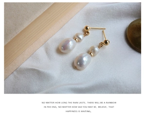 Close-up of baroque pearl drop earrings with gold metal accents on white silk