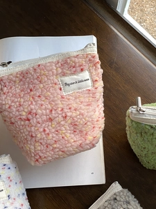 Dettaglio di pochette per trucco in peluche color pastello con cerniera e trama soffice