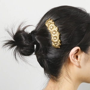 Minimalist golden sunflower hair clip accessory shown on model's dark hair side view