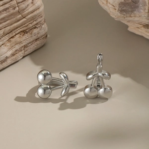 Close-up of silver cherry earrings with high-gloss mirror finish on wooden prop