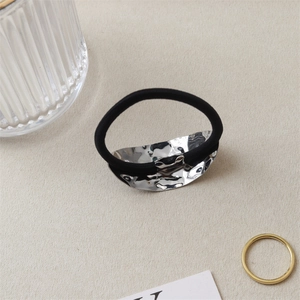 Detail of silver hammered metal hair tie with black elastic on beige fabric background