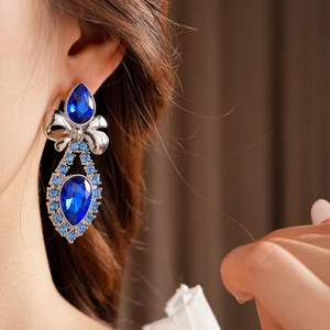 Close-up of a vintage silver bow earring with blue gemstones worn by a fashion model