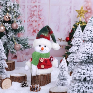 Cute plush Christmas snowman doll in festive plaid hat sitting on snowy wood decor
