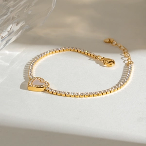 Detail van gouden harttennisarmband met schelpinleg op witte stenen achtergrond