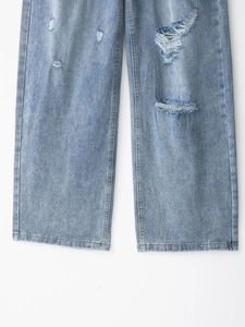 Dettaglio di jeans in denim lavato azzurro con strappi consumati e orlo della gamba dritto