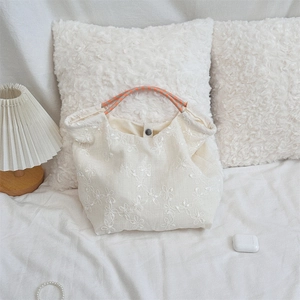 Close-up of white canvas tote bag with floral embroidery and orange woven handles