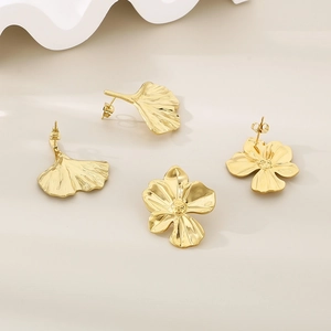 Macro detail of golden ginkgo leaf and five-petal flower stud earrings with hammered finish