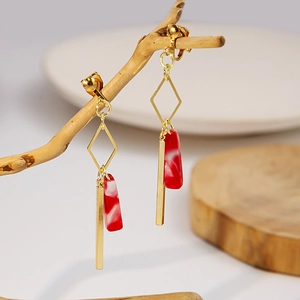 Macro detail of red marble resin earrings with gold accents on a natural wooden branch