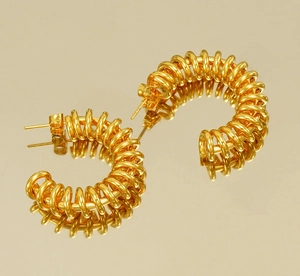 Detailed close-up of golden C-shaped spring earrings on a warm reflective surface