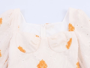 Detalle de escote cuadrado con bordado floral naranja y diseño calado elegante