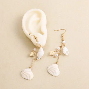 Detail view of bohemian shell and pearl tassel earrings hanging on a mannequin ear