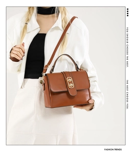 Close-up of brown leather handbag with gold oval twist lock and adjustable shoulder strap
