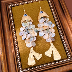 Detailed macro view of vintage fish-shaped earrings with shell scales and blue evil eye bead