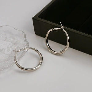 Detailed view of large silver hoop earrings on a display stand with a premium jewelry box