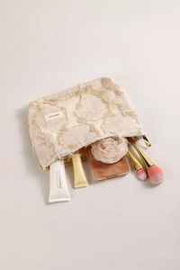 Detailed top view of a beige linen makeup bag with fringe and essential beauty tools