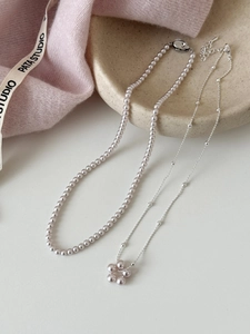 Détail du collier de perles avec pendentif fleur en argent posé sur un plat en céramique