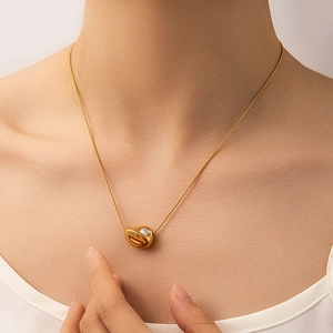 Dettaglio di una collana con ciondolo a fagiolo dorato e gemma bianca su modella