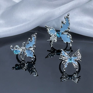 Three irregular silver butterfly rings with blue crystals on black reflective surface