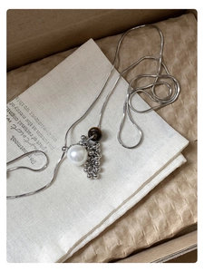 Detailed view of silver necklace with tiger eye stone and large white pearl pendant