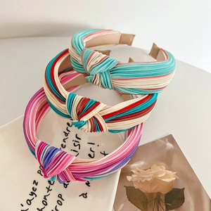 Three knotted striped fabric headbands in assorted colors displayed on a ceramic plate
