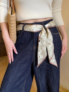 Detail of silk scarf belt with beige and gold paisley pattern on smooth satin fabric