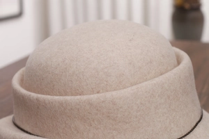Detail of wool cloche hat in beige featuring fine black bead chain and curled rim