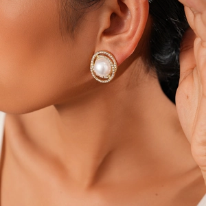 Close-up of elegant gold oval stud earring with white pearl and micro-pave crystals