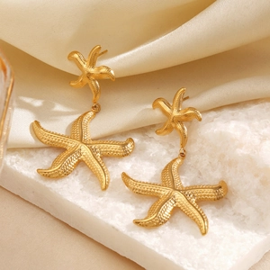 Golden starfish stud earrings for women on marble surface with beige silk background