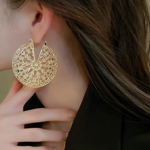 Gros plan d'une boucle d'oreille disque géométrique ajouré doré au motif complexe