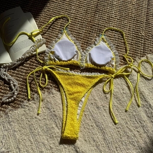 Flat lay of yellow bikini with white lace trim and textured fabric on a woven mat