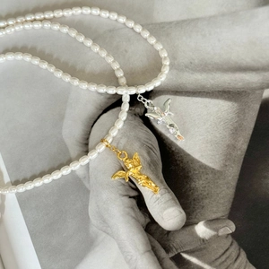Artistic detail of 925 silver angel pendants on a pearl necklace against a photo background