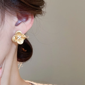 Close-up of golden flower stud earring with matte petals and cubic zirconia center