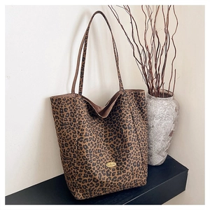 Detail of leopard print tote bag with golden Handmade emblem next to a minimalist vase