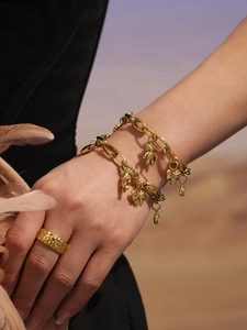 Close-up of gold chain bracelet with bear charm and textured hammer-finish ring