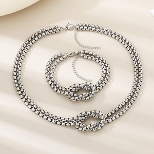 Detail of silver knot design necklace and bracelet set on a textured beige background