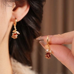 Gros plan de boucles d'oreilles fleur dorée avec rose en émail rouge et zircon sur l'oreille